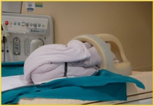 Il neonatino, coperto e monitorato sta per entrare nel magnete della Risonanza Magnetica mentre la sua testolina è già nella bobina.